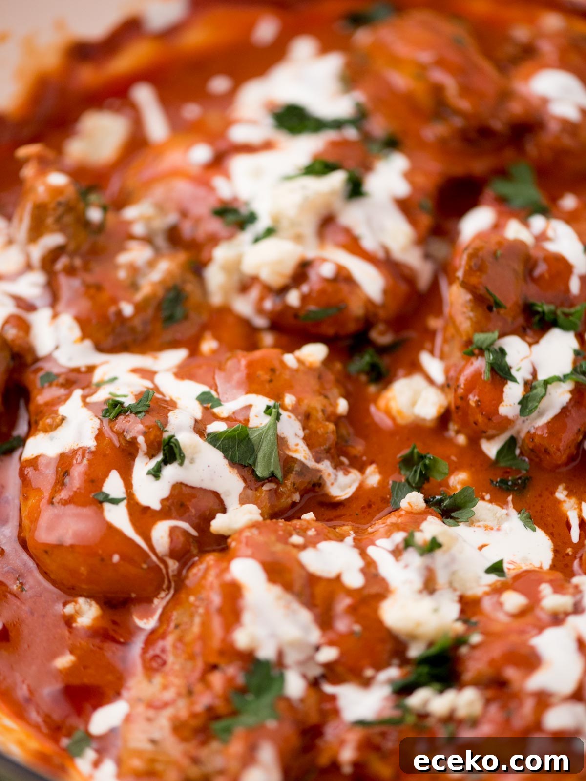 buffalo chicken thighs in a skillet surrounded by fresh parsley, a serving utensil, and a kitchen towel