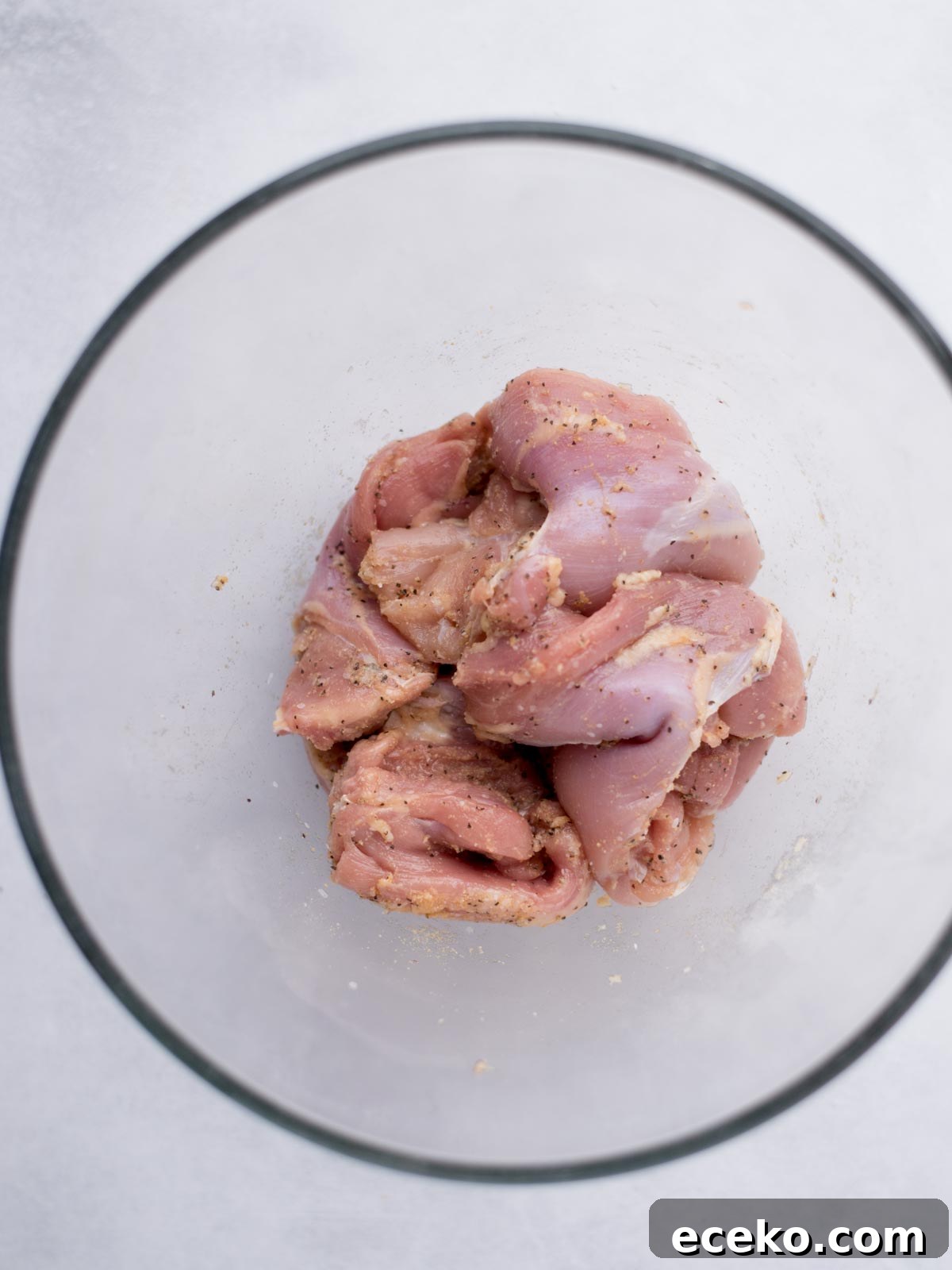 boneless skinless chicken thighs seasoned in a mixing bowl