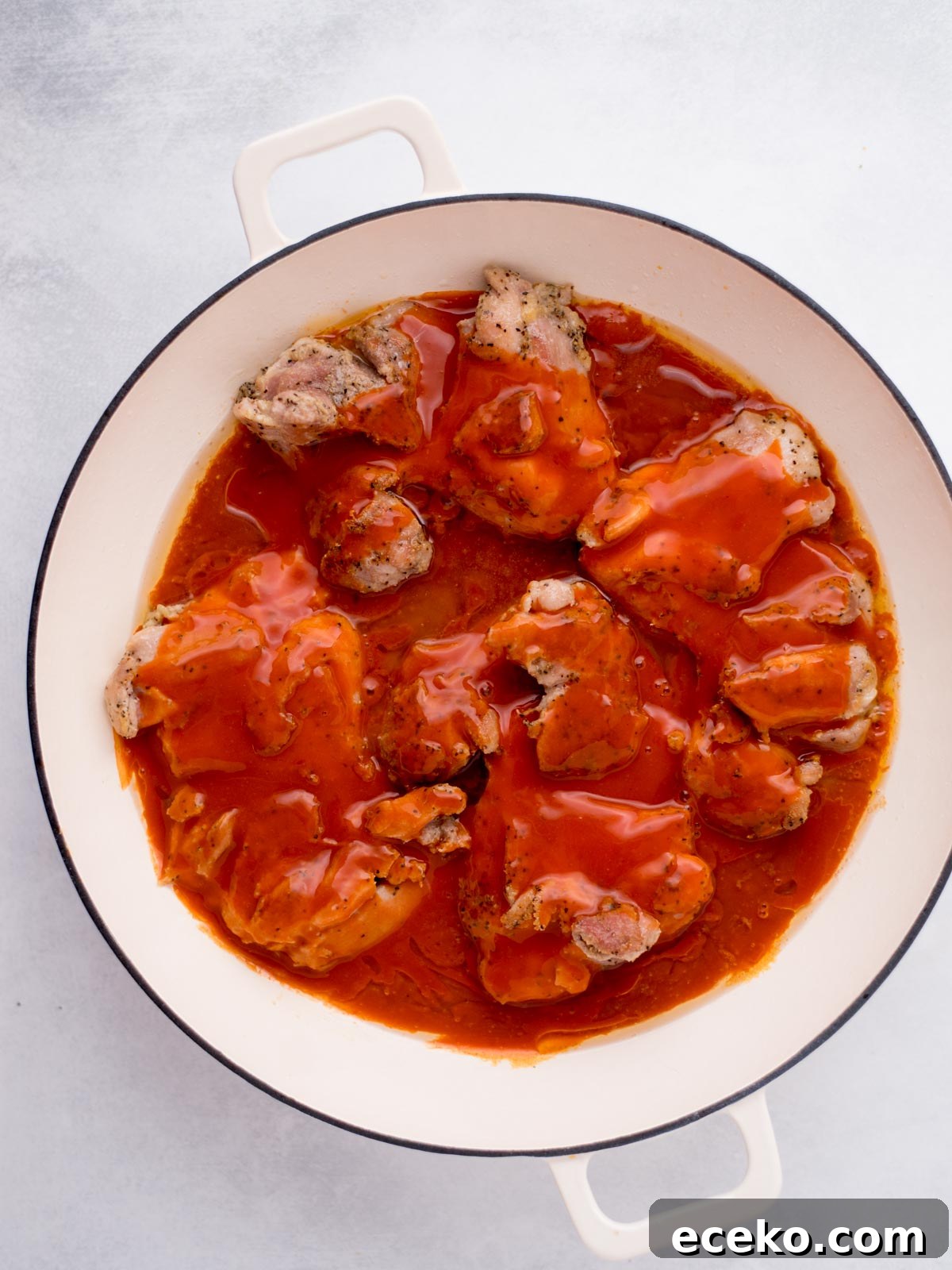 chicken thighs seared in a skillet topped with buffalo sauce