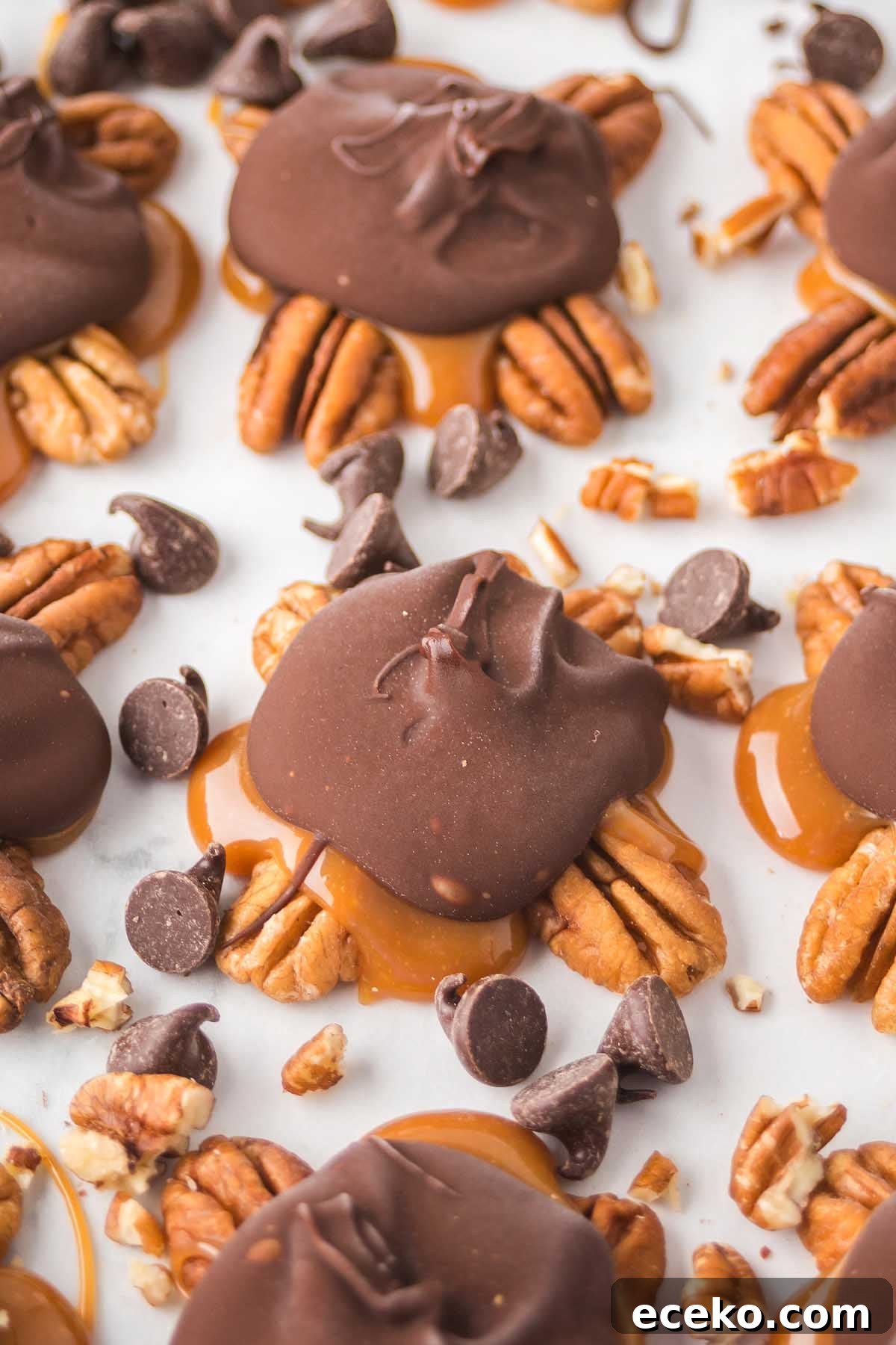 How to Make Classic Homemade Turtle Candies at Home 12 Close-up of homemade turtle candies featuring pecans, caramel, and chocolate, scattered with additional chocolate chips and chopped pecans on a white surface.