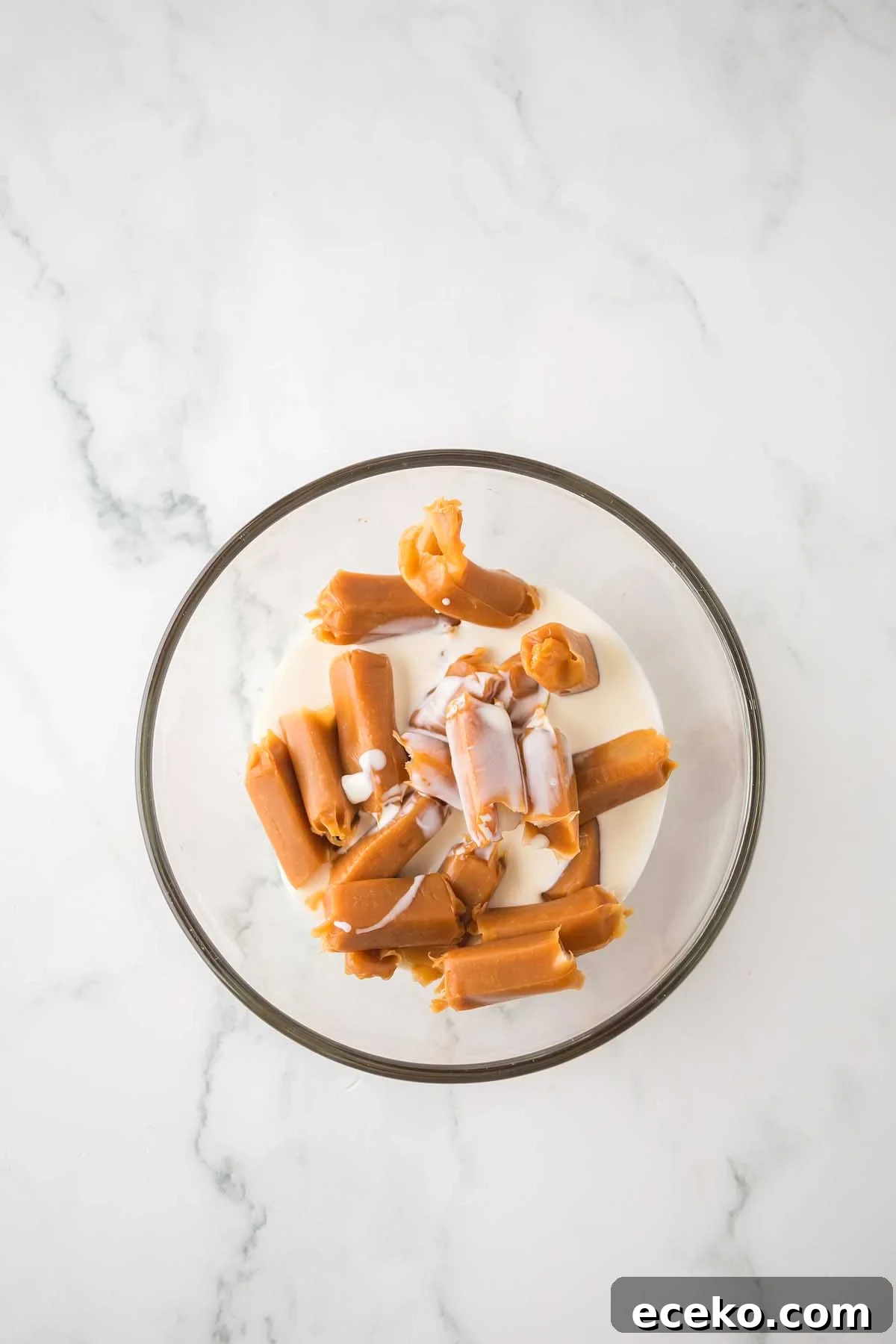 How to Make Classic Homemade Turtle Candies at Home 15 A clear bowl containing delicious homemade turtles, featuring cut sausage pieces bathing in a creamy white liquid, sits elegantly on a marble surface.
