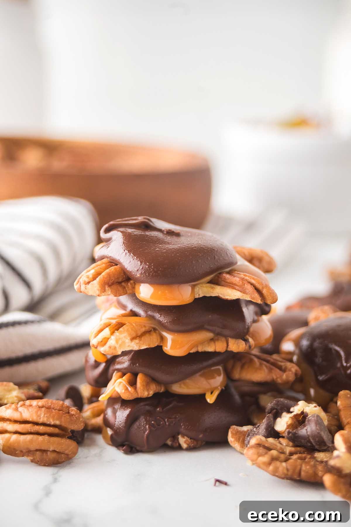 How to Make Classic Homemade Turtle Candies at Home 4 Homemade turtles are stacked with chocolate and caramel-coated pecans on a marble surface, complemented by a striped cloth in the background.