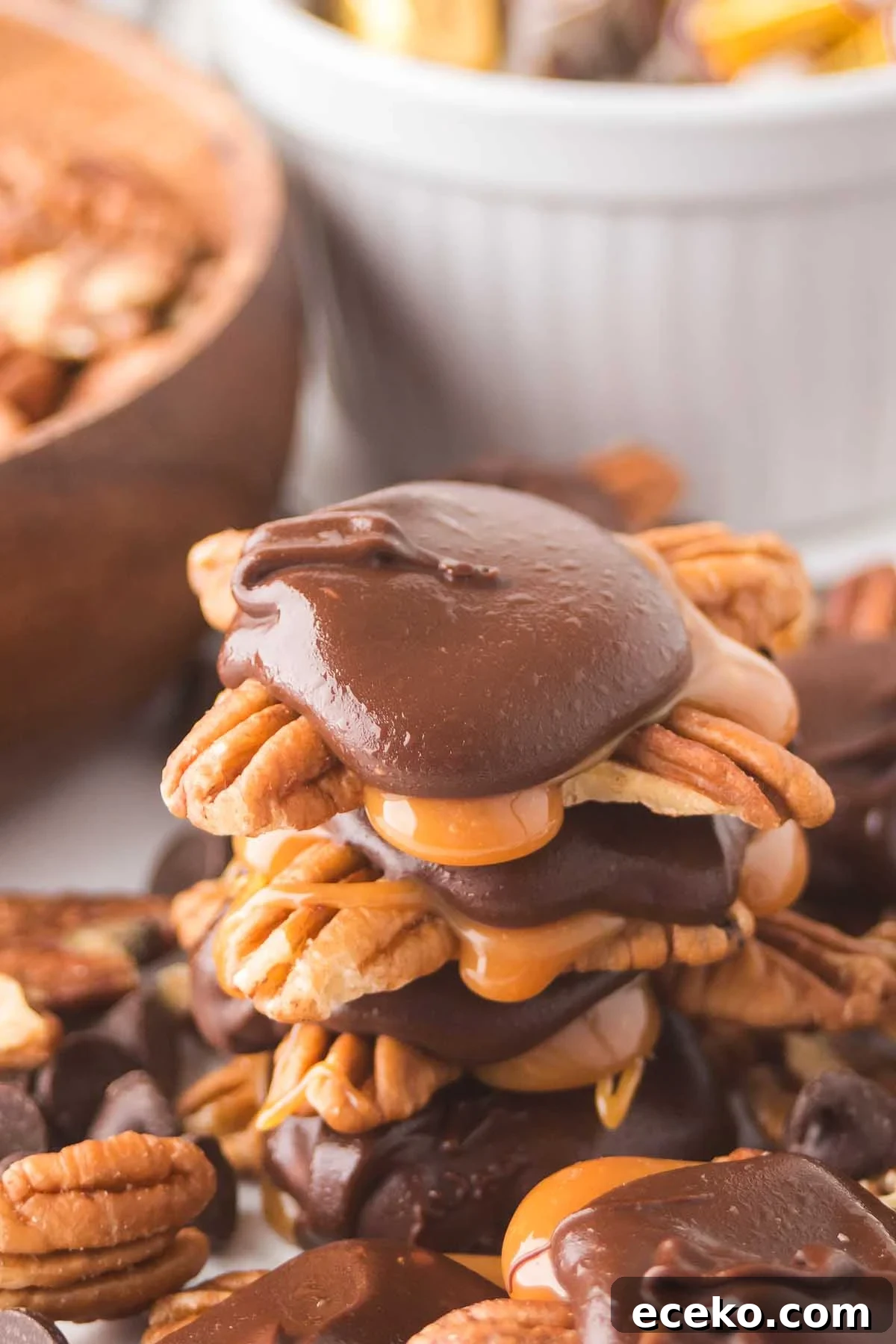 How to Make Classic Homemade Turtle Candies at Home 9 A stack of homemade turtles, rich with chocolate-covered caramel and pecan clusters, sits invitingly on the table with a bowl of mixed nuts in the background.