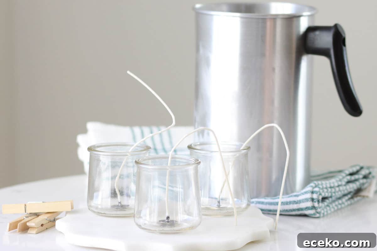 glass oui yogurt jars with candle wicks into them. a wax melting pot is sitting behind them on the table