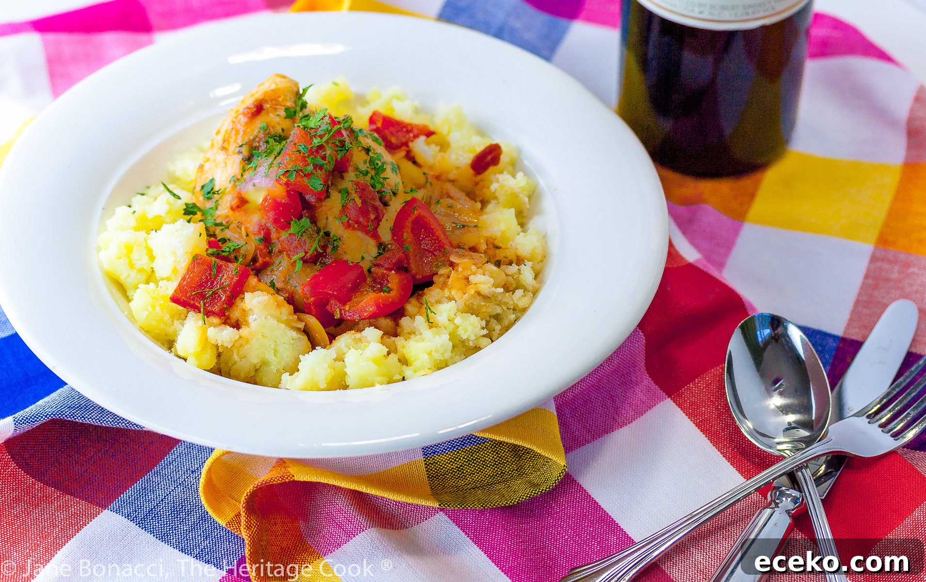 A white bowl with smashed yellow Yukon Gold potatoes is topped with chicken braised in tomatoes, onions, mushrooms, and wine; Comforting Chicken Cacciatore with smashed Yukon Gold potatoes © 2023 Jane Bonacci, The Heritage Cook. 