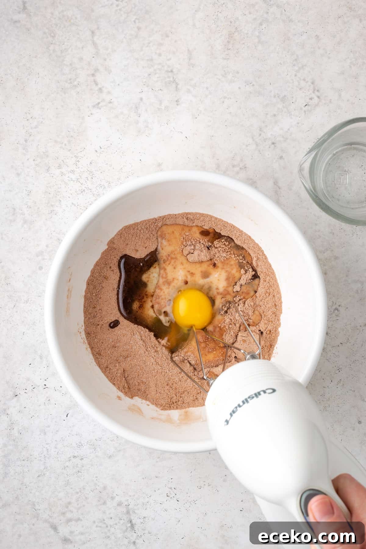 Egg, milk, vanilla and oil being mixed into the dry ingredients with a handheld mixer.