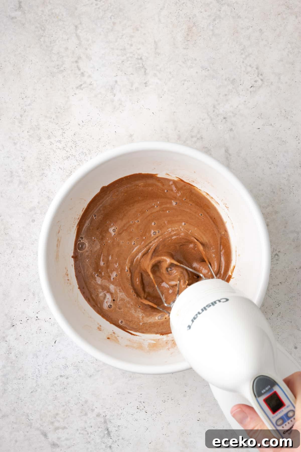Hot water being beaten into the cake batter in a large white bowl.