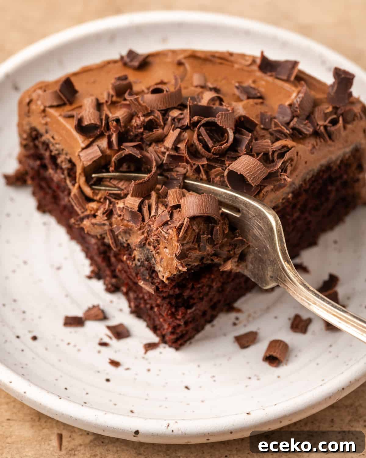 A slice of chocolate cake topped with chocolate frosting and chocolate shavings.