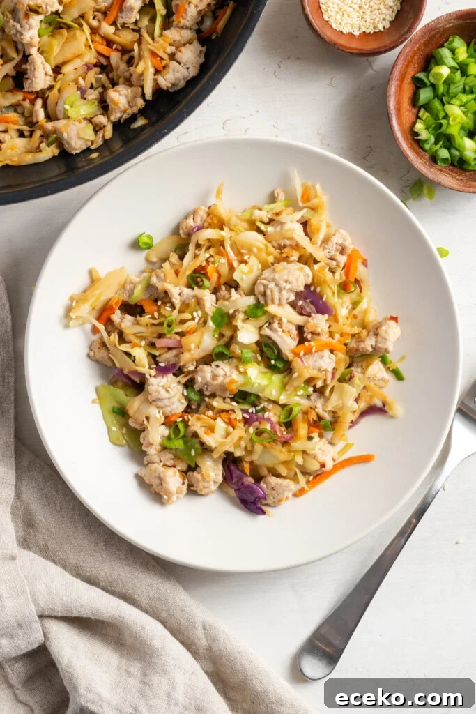 white pasta bowl of ground turkey egg roll in a bowl on a white table with a silver fork, a pinch bowl of scallions and a pinch bowl of sesame seeds, with a white cloth napkin.