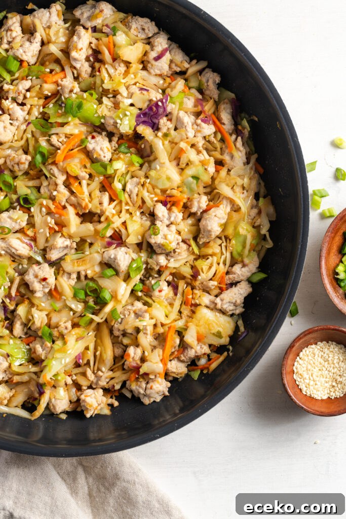 closeup shot of healthy turkey egg roll in a bowl cooking in a black skillet on a white table with scallions scattered around.