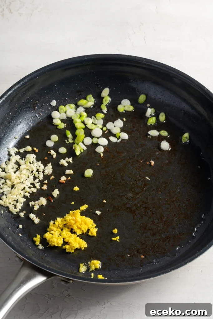 scallion whites and pale greens, ginger, and garlic sautéing in a pan with oil.