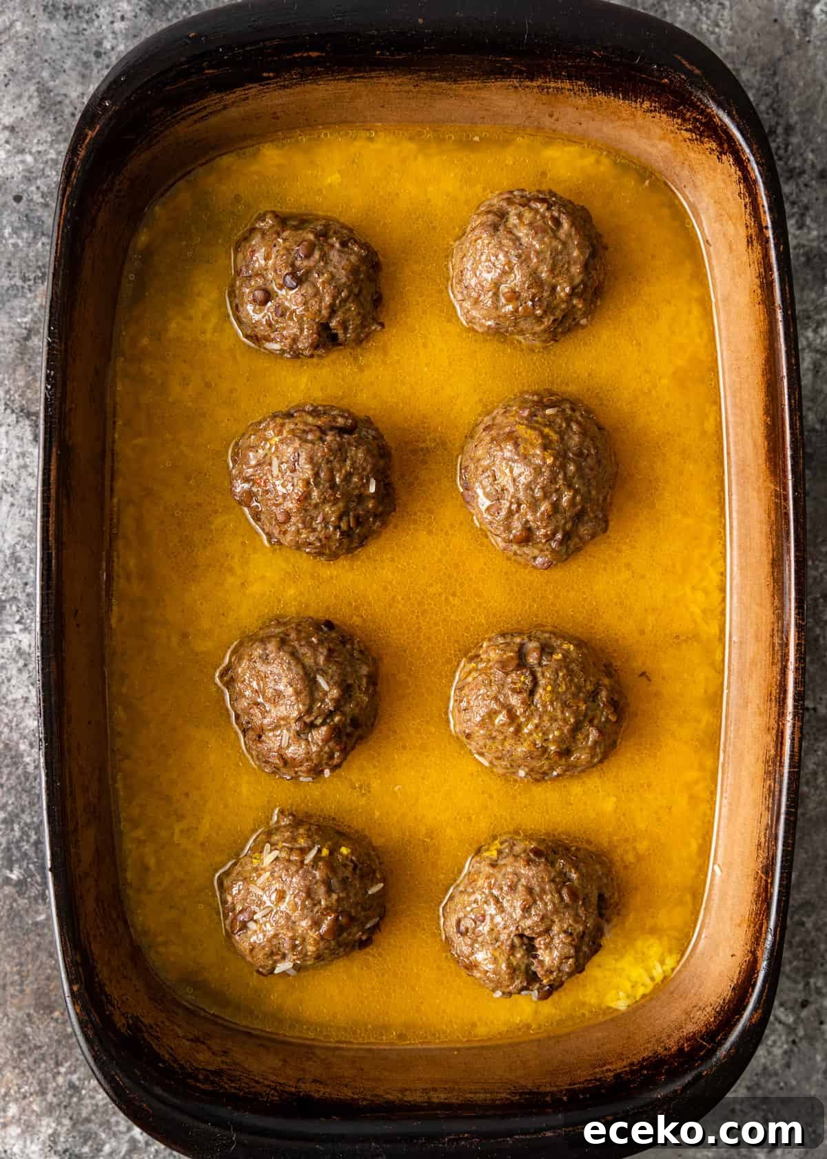 Savory Lamb and Lentil Meatballs with Zesty Lemon Rice 8 overhead process shot: lamb meatballs in a baking dish with lemon broth