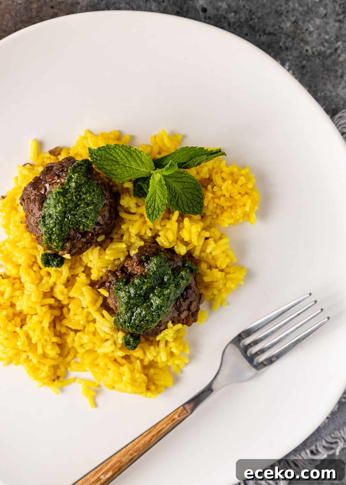 Savory Lamb and Lentil Meatballs with Zesty Lemon Rice 10 overhead: two lamb meatballs over lemon rice with mint pesto on a white plate with a fork