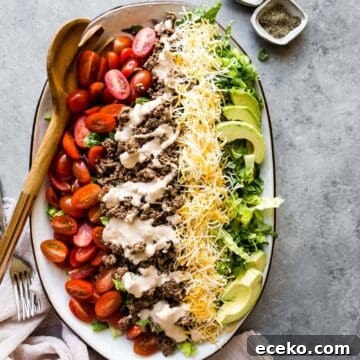 taco salad on a platter with tomatoes, shredded cheese, and avocado slices