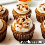 Six frosted carrot cake cupcakes topped with cream cheese frosting, chopped pecans, and finely grated carrots