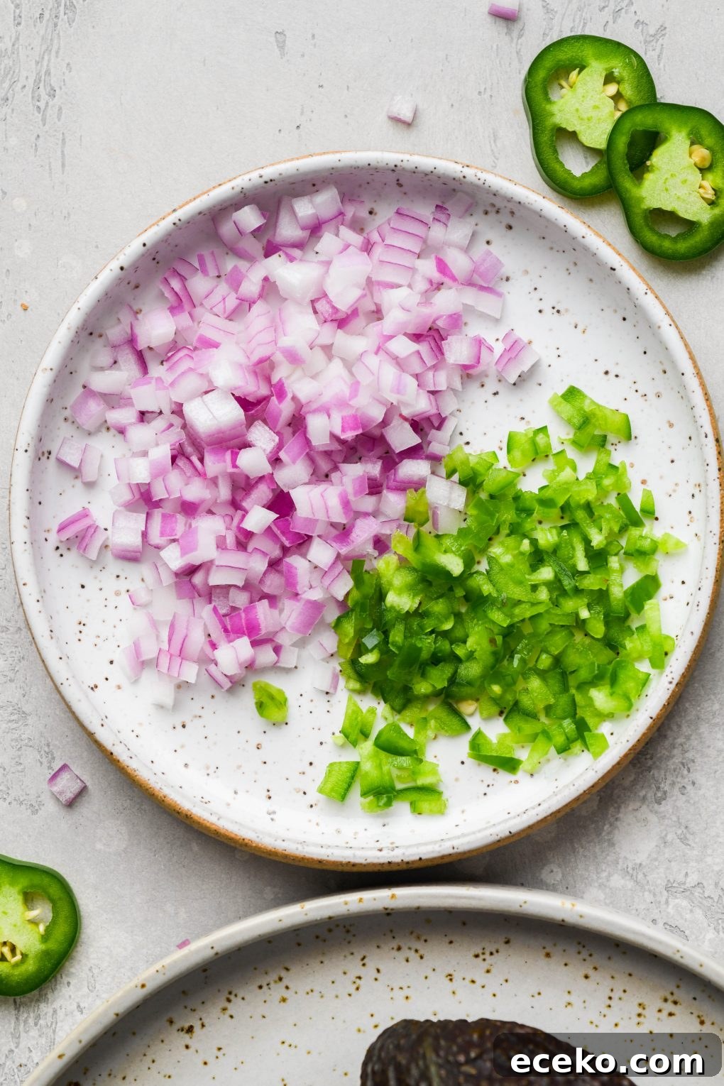 Close up image of a small white speckled plate with finely diced red onion and jalapeno. On a light grey background.