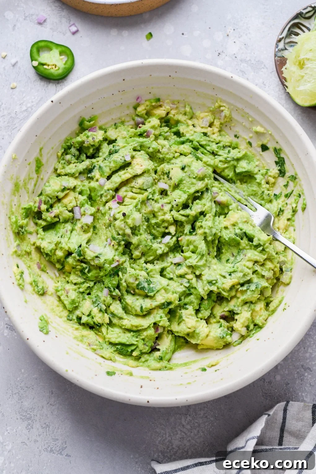 Image of easy guacamole smashed together with the other ingredients. On a light grey background. 