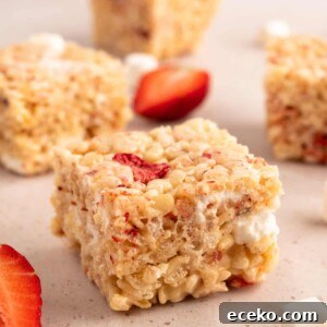 Strawberry Rice Krispie Treats Recipe for Fresh, Fruity Squares 11 cut strawberry rice krispie treat squares on a beige background with strawberry wedges and miniature marshmallows