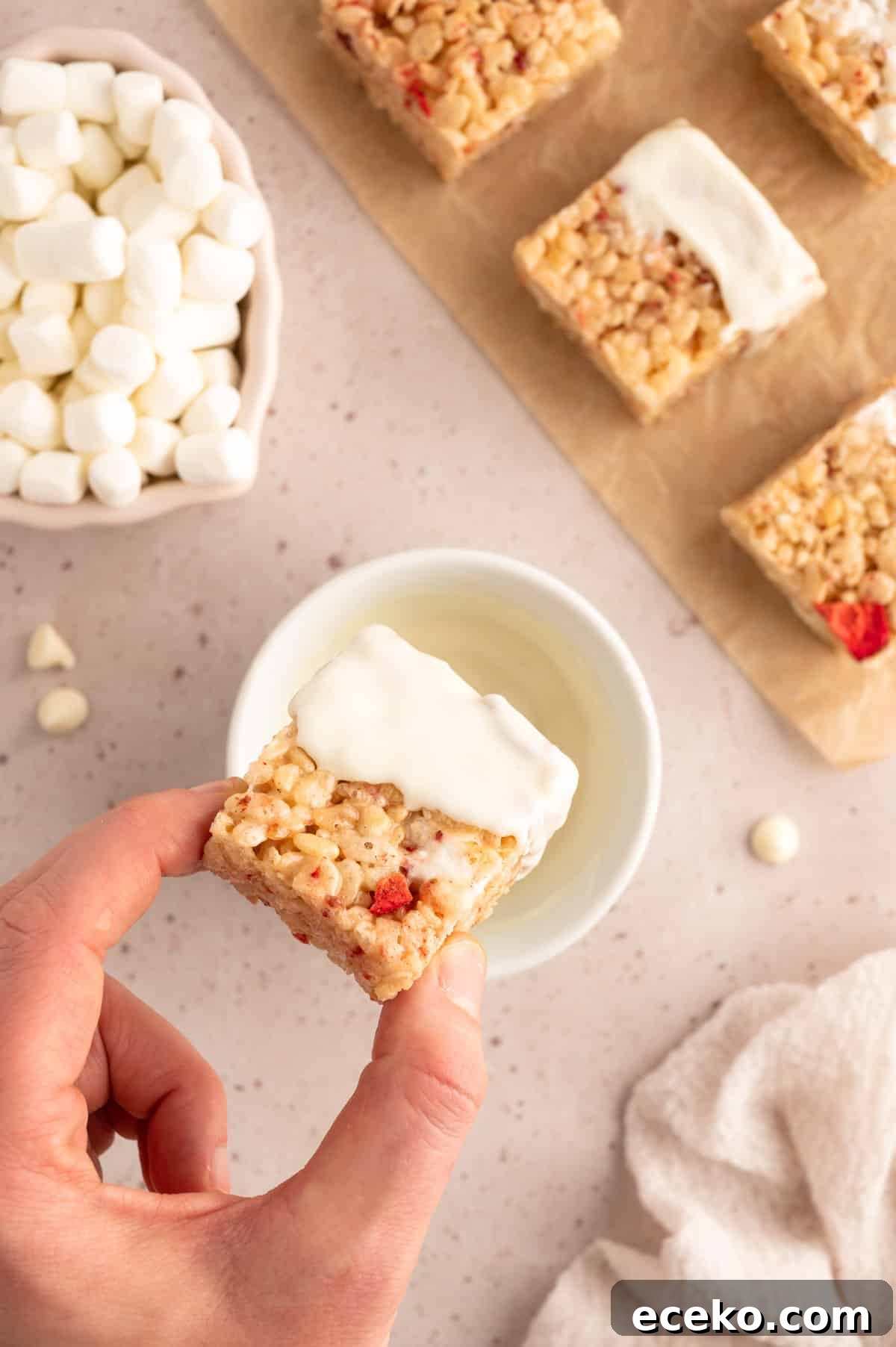 Strawberry Rice Krispie Treats Recipe for Fresh, Fruity Squares 9 overhead photo of a cut strawberry rice krispie treat being dipped into a bowl of melted white chocolate