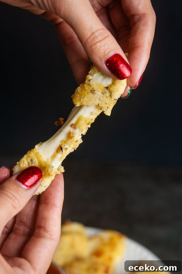 Low carb mozzarella stick being stretched apart by two female hands on black