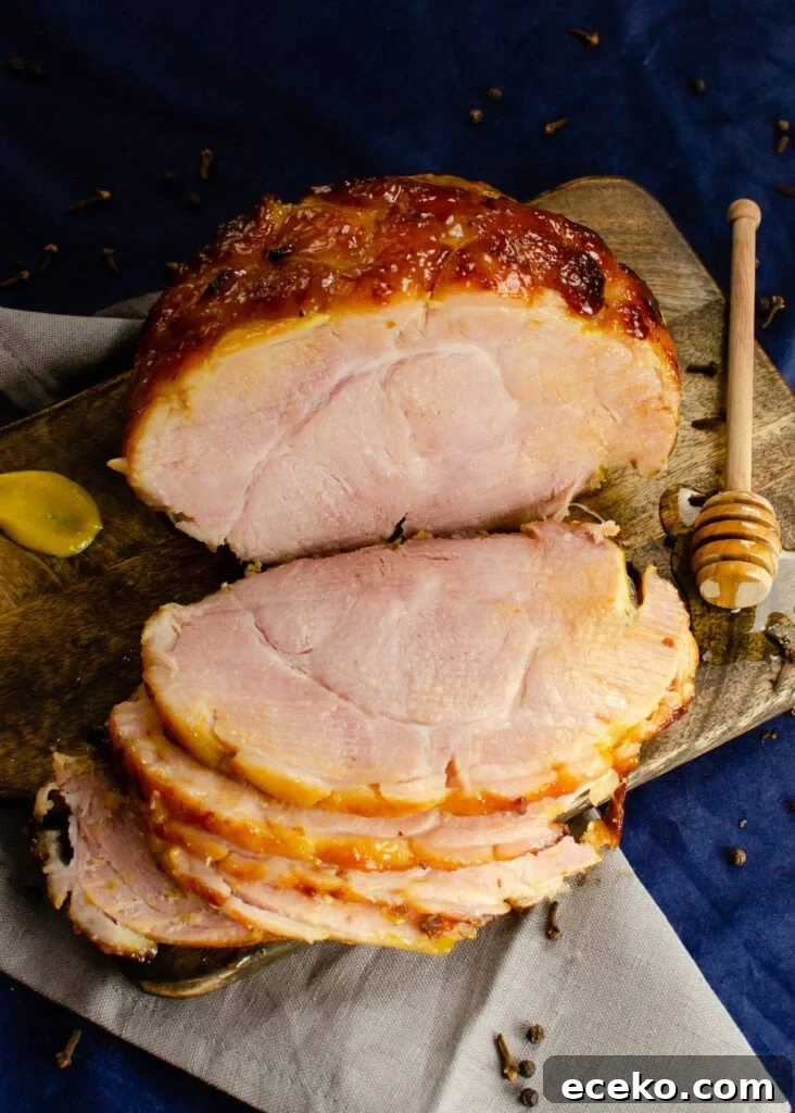 Honey-Glazed Roast Gammon Joint Recipe 2 Honey Roast ham joint on a wooden board with three slices cut from it with a honey stick coated in honey and a dollop of mustard on the sides