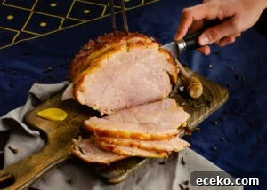 Honey-Glazed Roast Gammon Joint Recipe 11 Cutting slices of the honey roast gammon joint on a wooden chopping board with a silver knife and a meat fork holding the joint in place