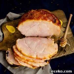 Honey-Glazed Roast Gammon Joint Recipe 3 Honey Roast ham joint coated in a honey and mustard glaze on a wooden board with three slices cut from it with a honey stick coated in honey and a dollop of mustard on the sides