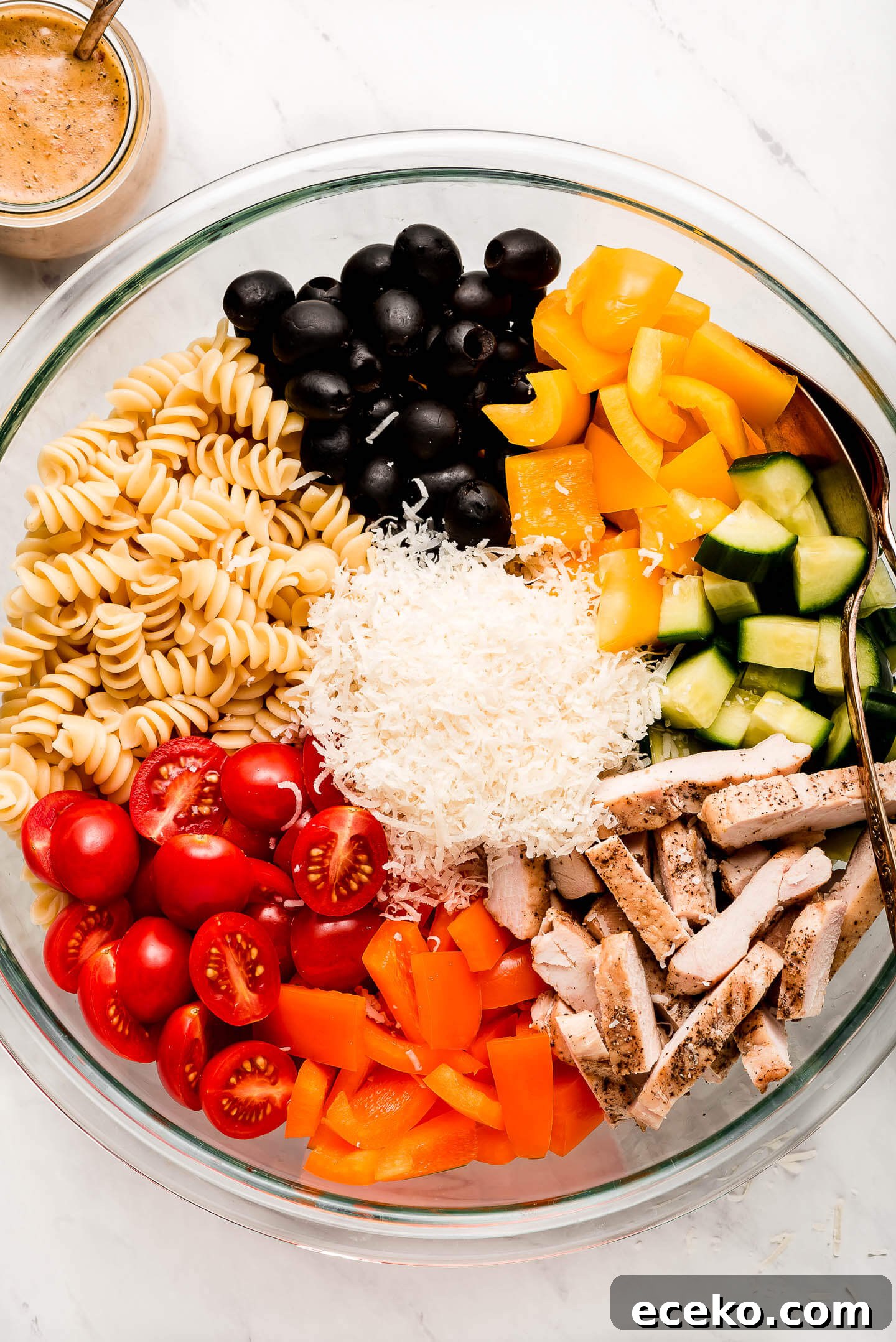 Creamy Chicken and Vegetable Pasta Salad Recipe 3 A bowl of separated ingredients- olives, peppers, cucumbers, grilled chicken, tomatoes, and pasta.