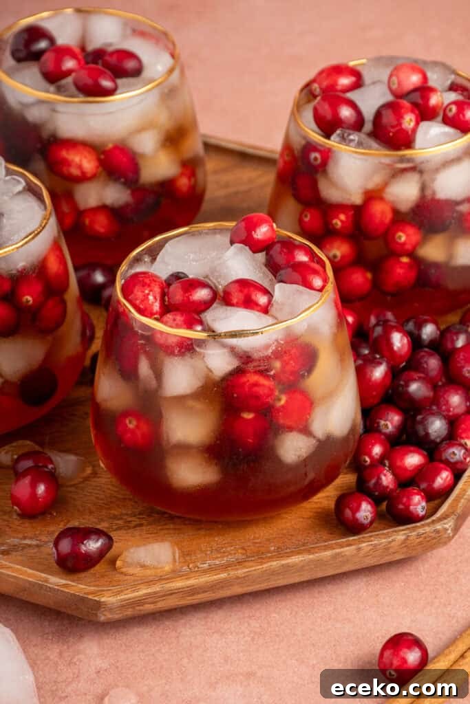 Close up of a glass with ice, cranberries, and cranberry chai mocktail on a wood platter.