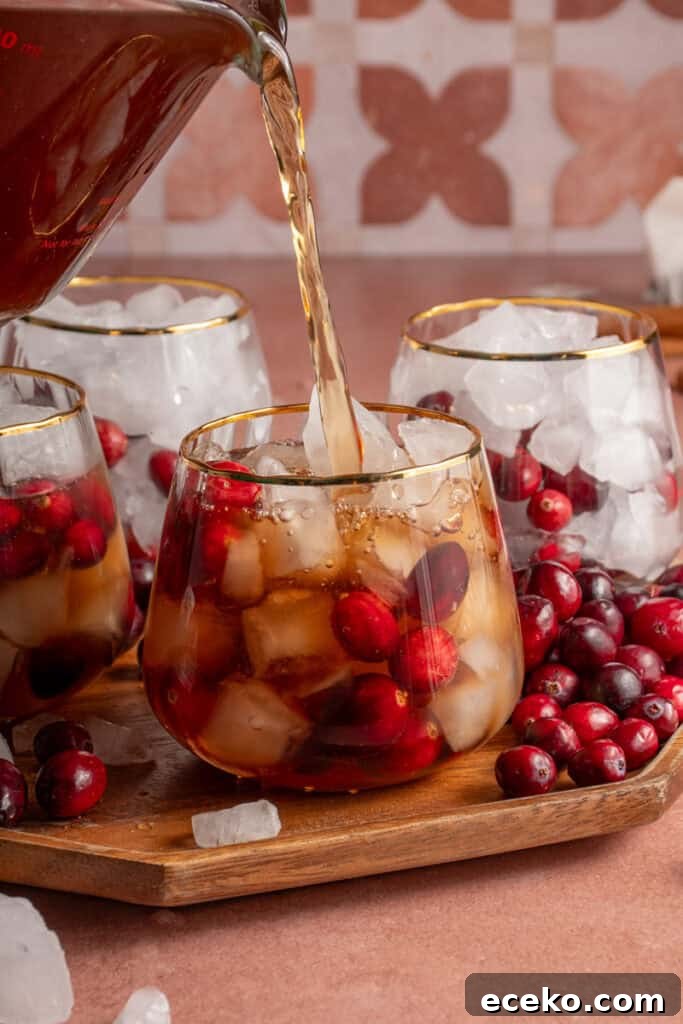 Cranberry Chai Mocktail being poured into a glass with ice and fresh cranberries.