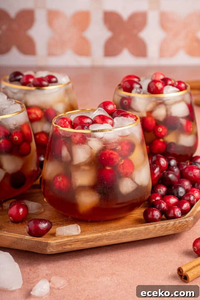 Glasses on a wood platter filled with ice, fresh cranberries, and Cranberry Chai Mocktail.