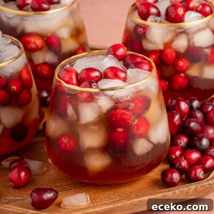 Four glasses on a platter filled with ice, cranberries, and Cranberry Chai Mocktail.