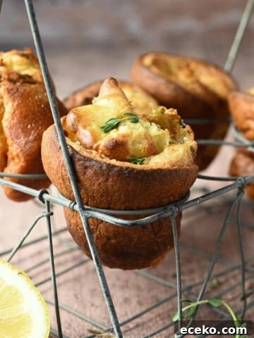 Lemon popovers are suspended in a wire rack with thyme and lemons in the forefront.