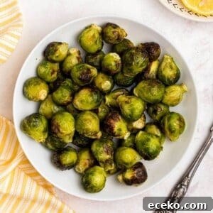 Green and juicy brussels sprouts in a white bowl in front of an air fryer with lemon slices on a plate.