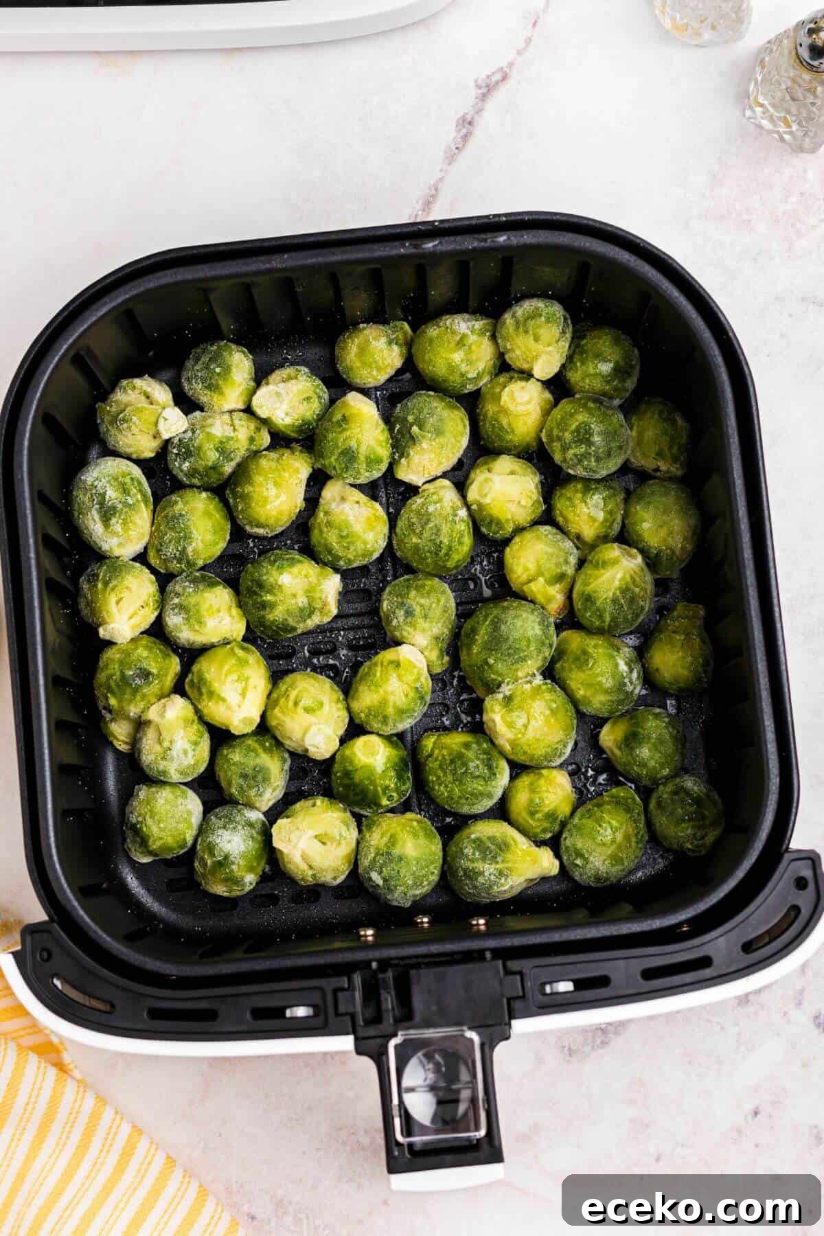Frozen brussels sprouts in the air fryer basket before being cooked. 