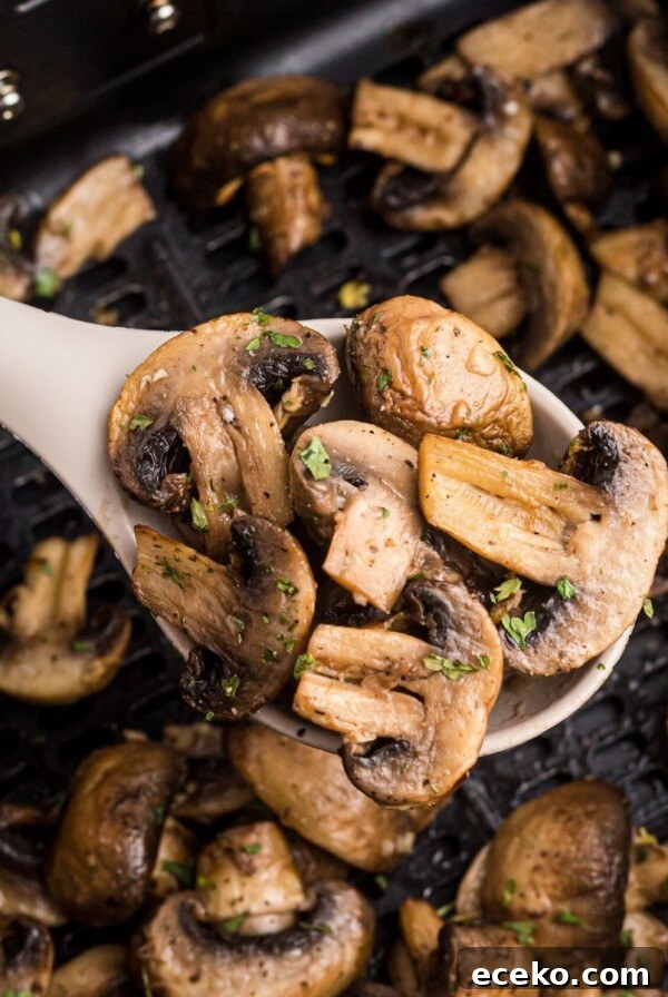 A spoonful of air fryer mushrooms held up over the pan of more.