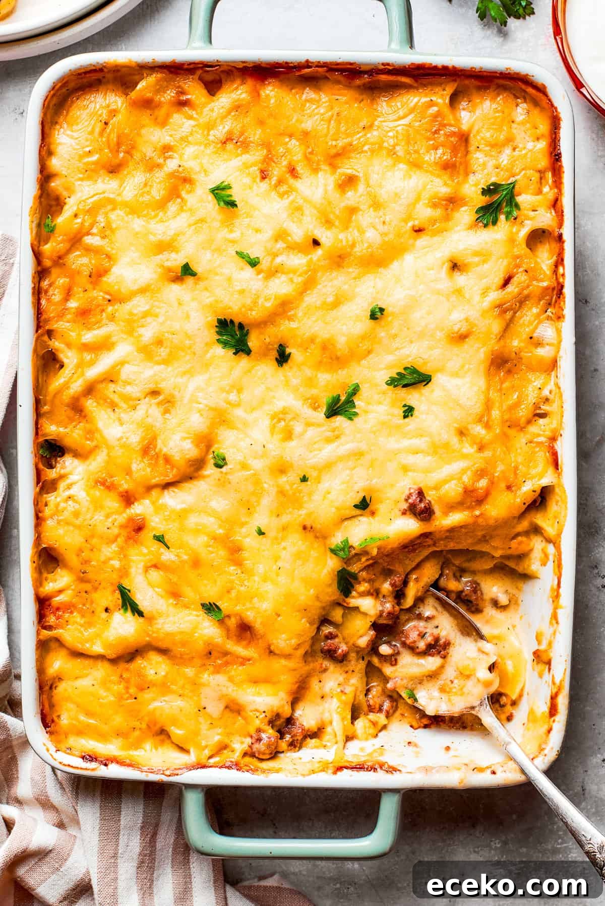 Overhead image of hamburger potato casserole in a baking dish, with a serving of it missing from the corner.