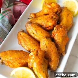 Oven-baked lemon pepper wings coated in a zesty buttery sauce, served with lemon slices.
