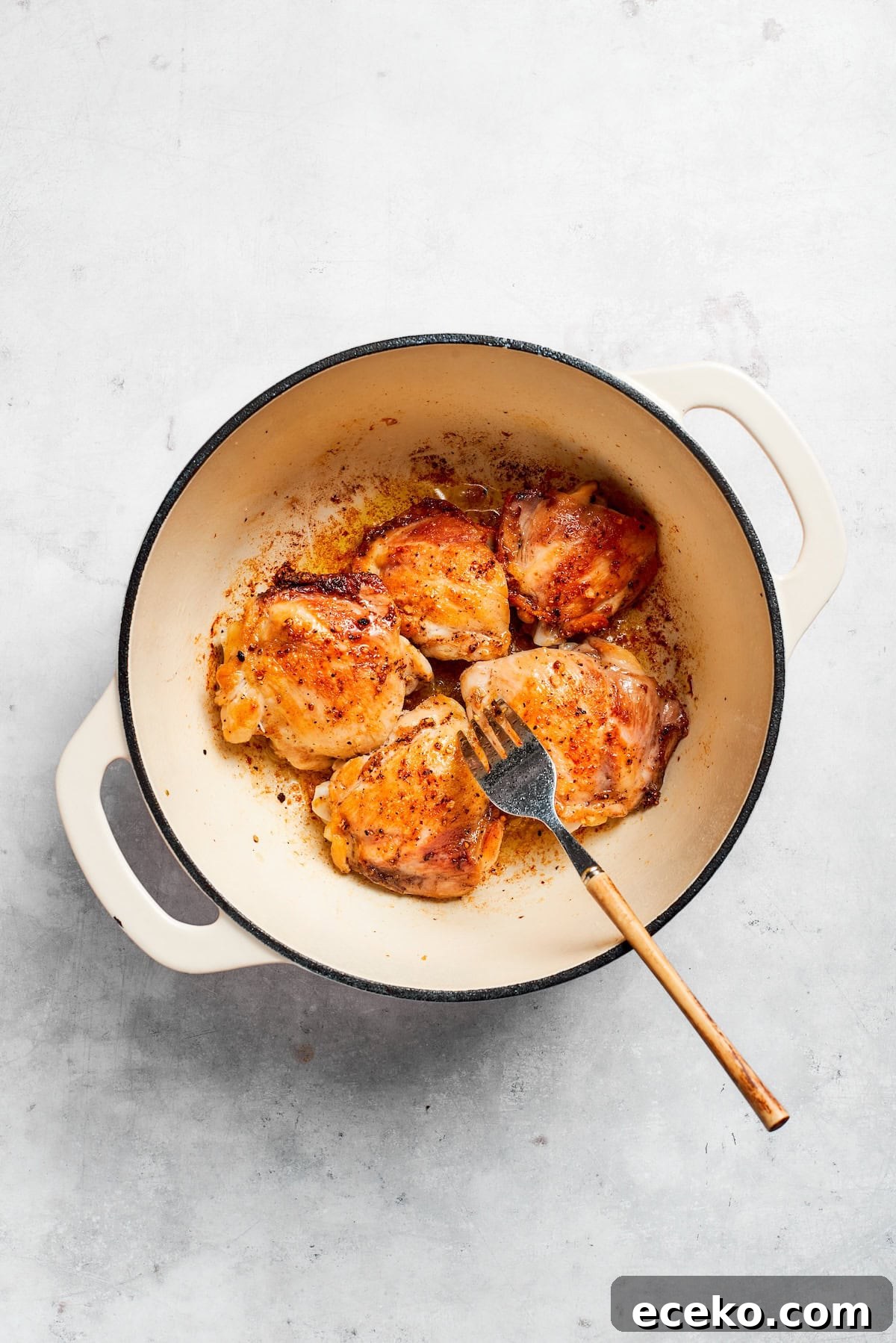 Brown the chicken in a pot. A fork moves chicken in a pot.