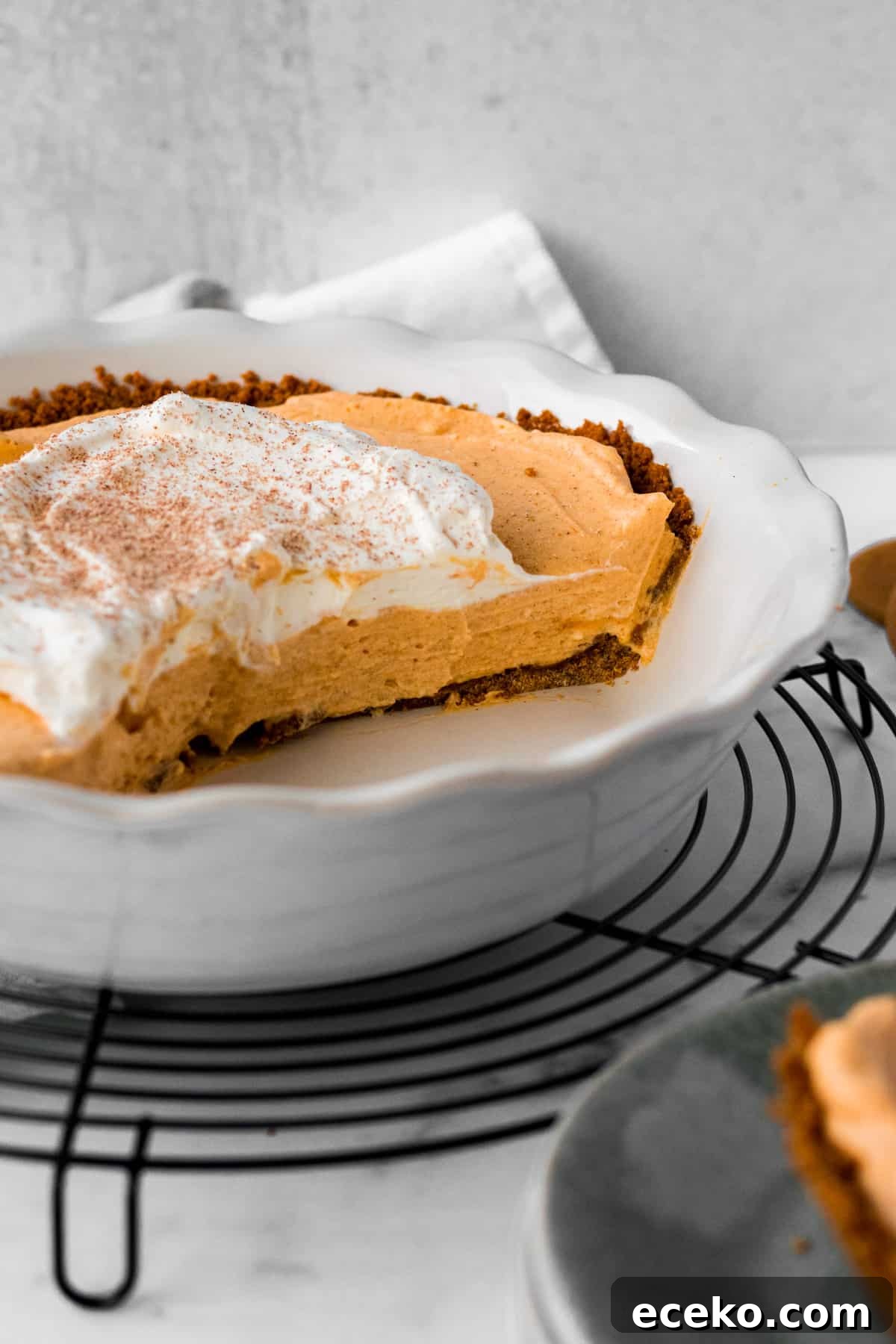 Gingersnap Crust Pumpkin Mousse Pie: Creamy Autumn Dessert 3 white pie dish on circular cooling rack with half a pumpkin mousse pie inside