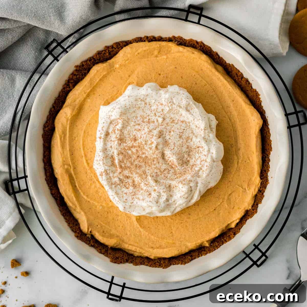 pumpkin mousse pie in white pie dish on black cooling rack with pie server and gingersnap cookies
