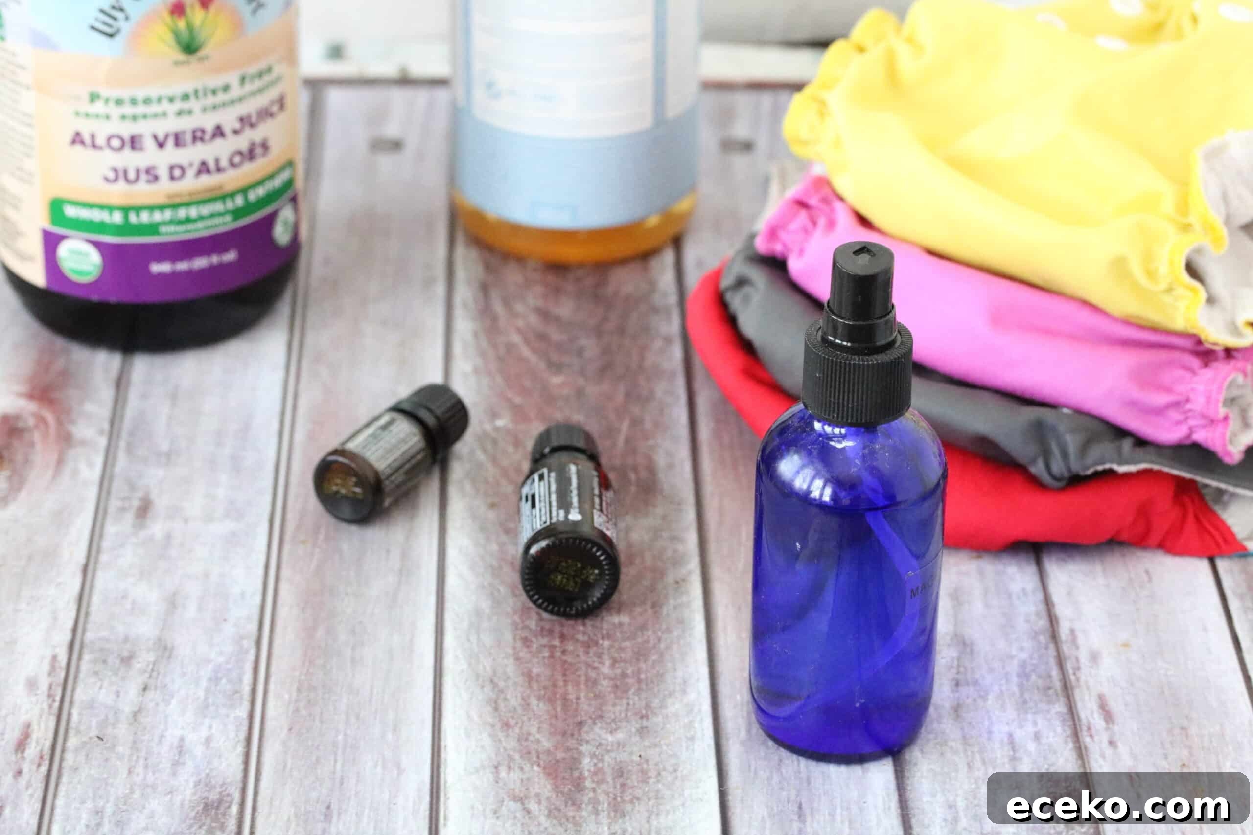 a cobalt blue bottle surrounded by ingredients like essential oils and aloe as well as cloth diapers
