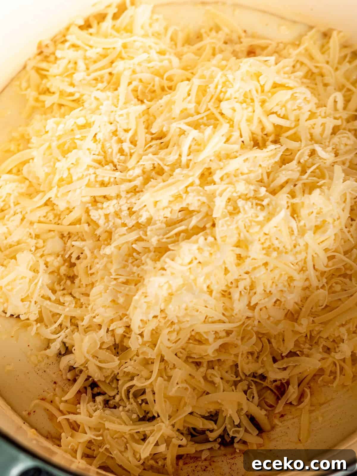 Shredded cheese in a large pot of roux.