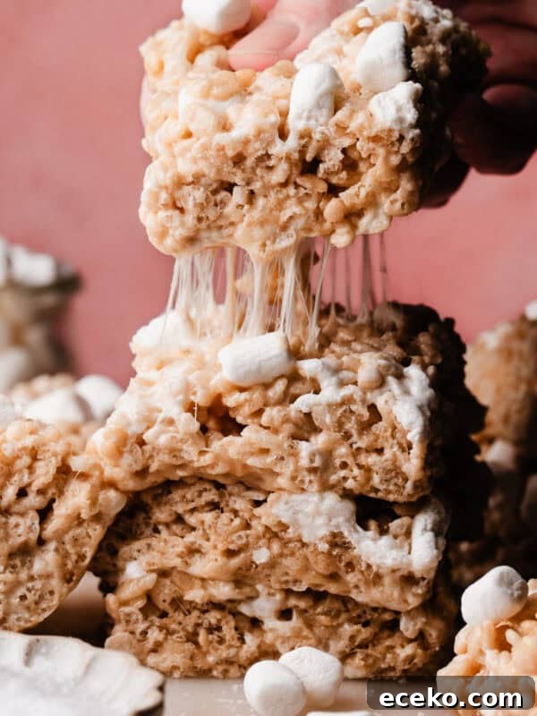 No-Bake Edible Cookie Dough Bites Recipe for Parties 12 A stack of rice krispie squares, with the top one being lifted away, leaving a trail of gooey marshmallow strands behind.