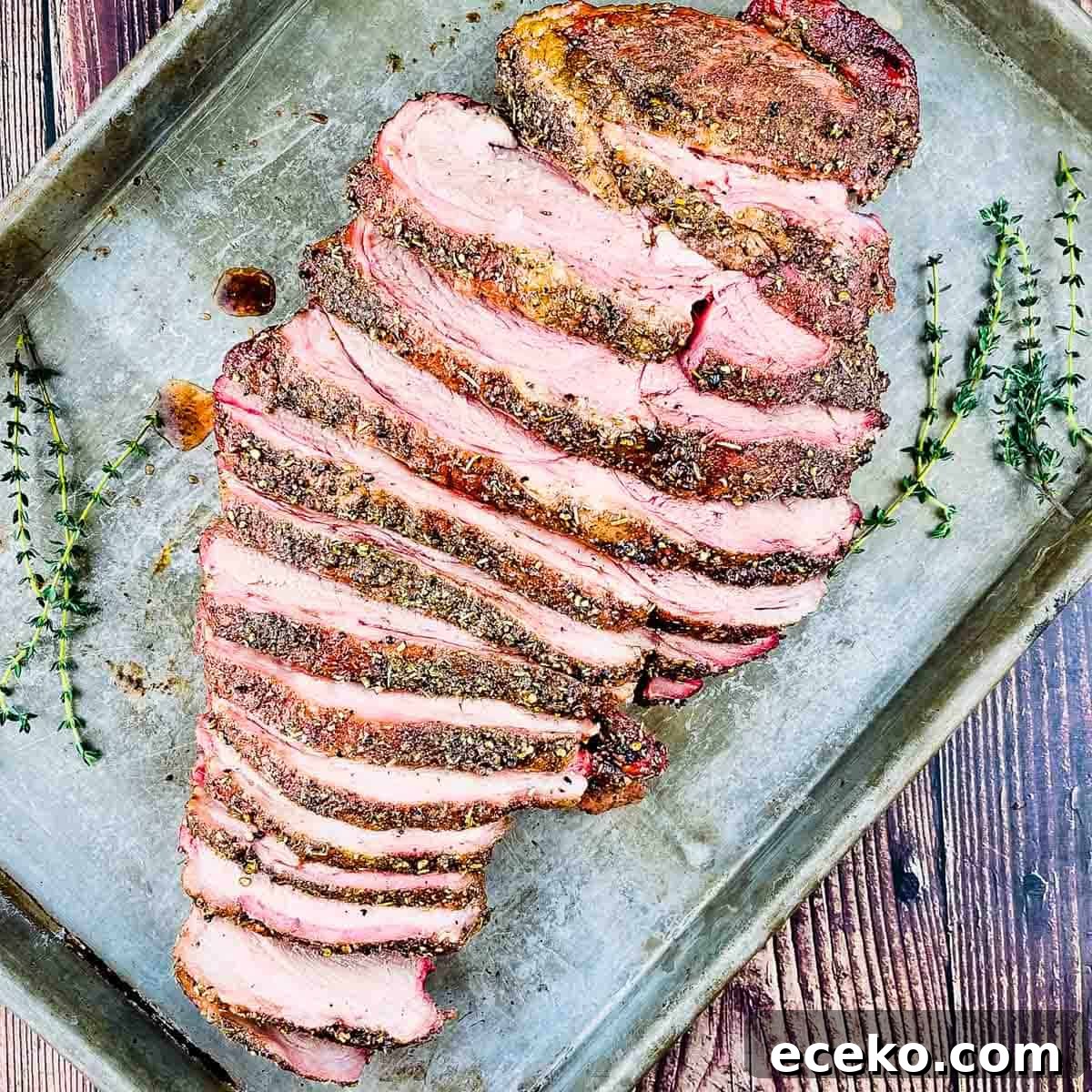 Boneless Smoked Leg of Lamb on a Pellet Grill — Tender Recipe 2 Smoked boneless leg of lamb sliced and placed on a baking sheet with sprigs of fresh rosemary beside it.