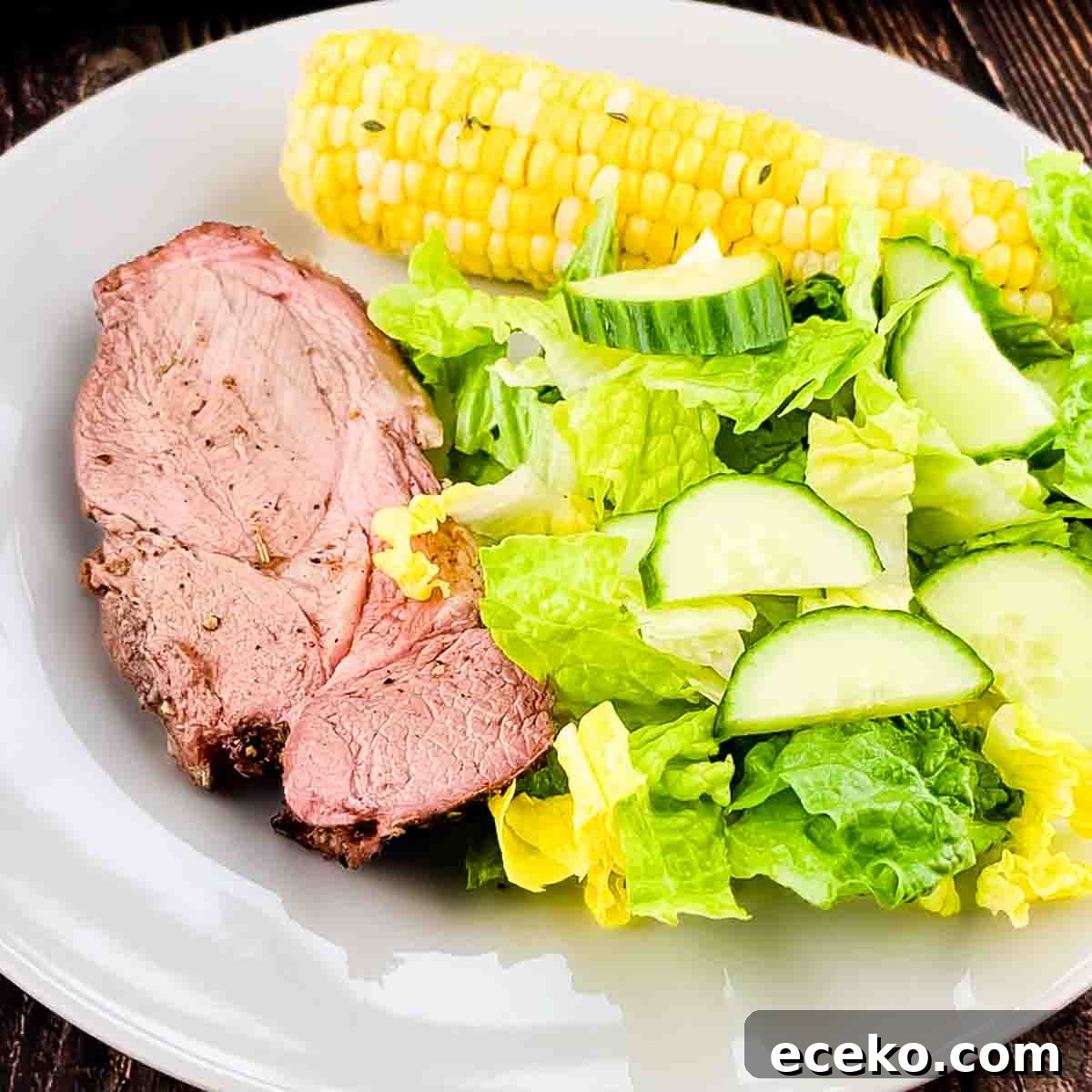 Boneless Smoked Leg of Lamb on a Pellet Grill — Tender Recipe 11 A slice of smoked leg of lamb on a white plate with a green salad and smoked corn on the cob.