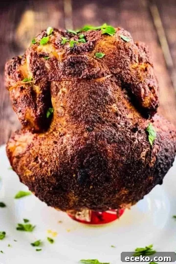 Smoked beer can chicken placed on a white serving dish, sprinkled with parsley.