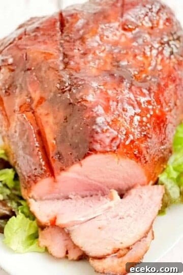 Double smoked ham on white platter, covered in glaze, with green lettuce for garnish.