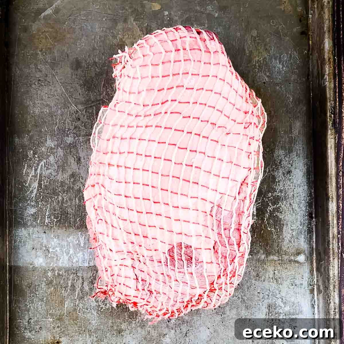 Boneless Smoked Leg of Lamb on a Pellet Grill — Tender Recipe 4 A leg of lamb with the netting still on, placed on a baking sheet.