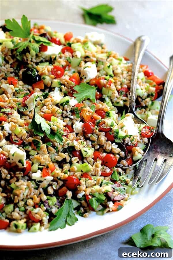 Close-up photo of Mediterranean Farro Salad on white platter with serving utensils.